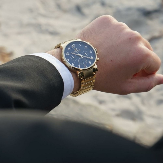 Oryginalny zegarek męski marki Tommy Hilfiger na złotej, stalowej bransolecie. Złote wskazówki i indeksy na niebieskiej/granatowej, analogowej tarczy z chronografami - 24h, dzień tygodnia i miesiąca. Cyfry arabskie. Złota koperta zegarka o średnicy 44 mm.