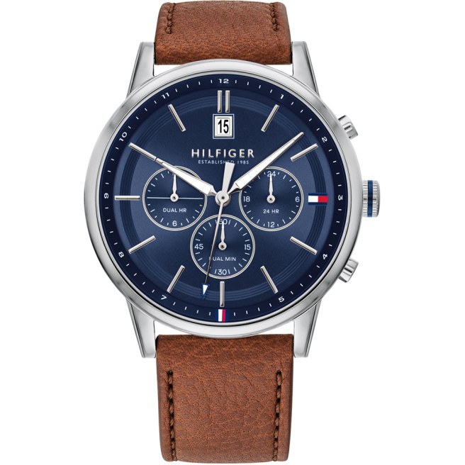 Zegarek męski marki Tommy Hilfiger na brązowym skórzanym pasku. Srebrne indeksy, fluorescencyjne wskazówki i sekundnik na granatowej tarczy z chronografami i datownikiem. Srebrna koperta zegarka o średnicy 44 mm.